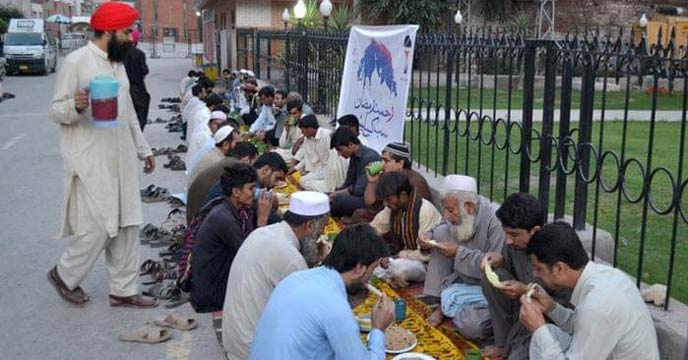 A group of people, including men, women, and children, are sitting together on the ground and having food in an open field.