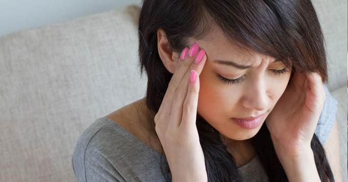 A young woman holding her head in pain, possibly experiencing a migraine